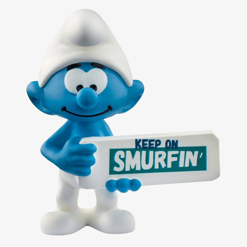 Mini figurine Schtroumpf Schleich de 5 cm avec panneau "Keep on Smurfin'" dans une scène colorée et détaillée.